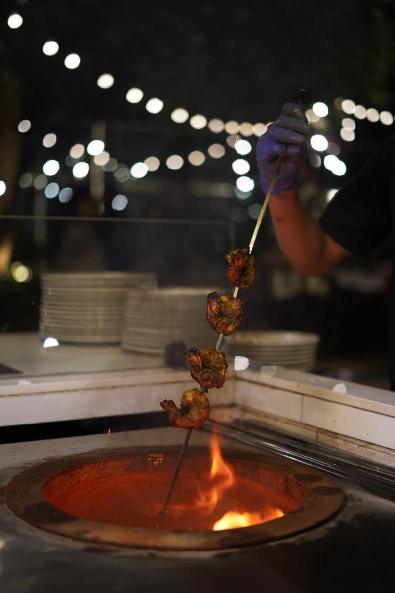 a person cooking food on a stick in a pot of fire at Courtyard by Marriott Gurugram Downtown in Gurgaon
