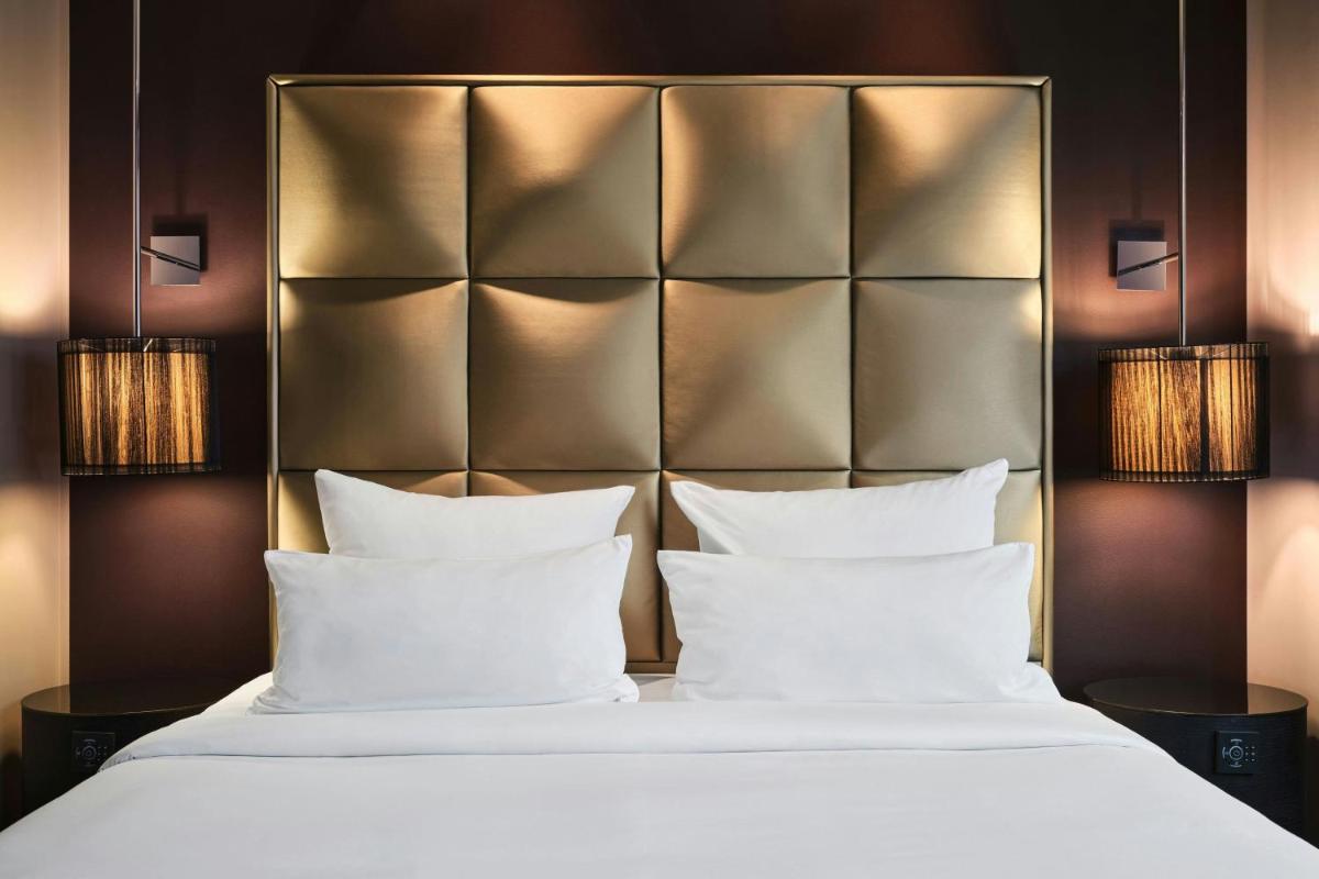 ein Schlafzimmer mit einem Bett mit weißen Kissen und Lampen in der Unterkunft Roomers Frankfurt Central, Autograph Collection in Frankfurt am Main