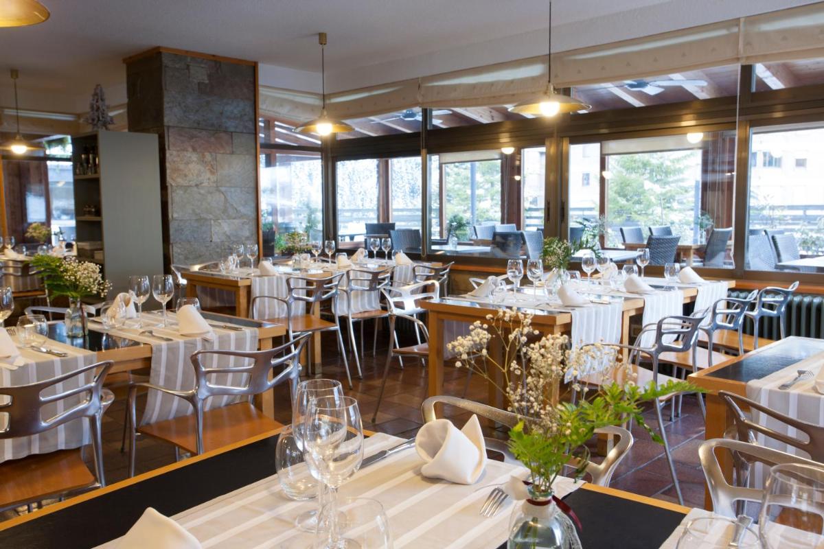 Un restaurante con mesas y sillas blancas y ventanas. en Tuc Blanc, en Baqueira Beret