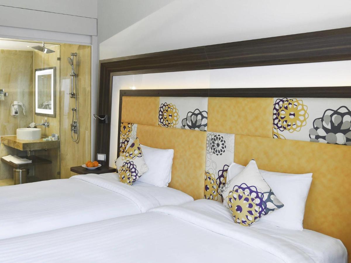 a bedroom with a large white bed and a bathroom at Novotel Pune Viman Nagar Road in Pune