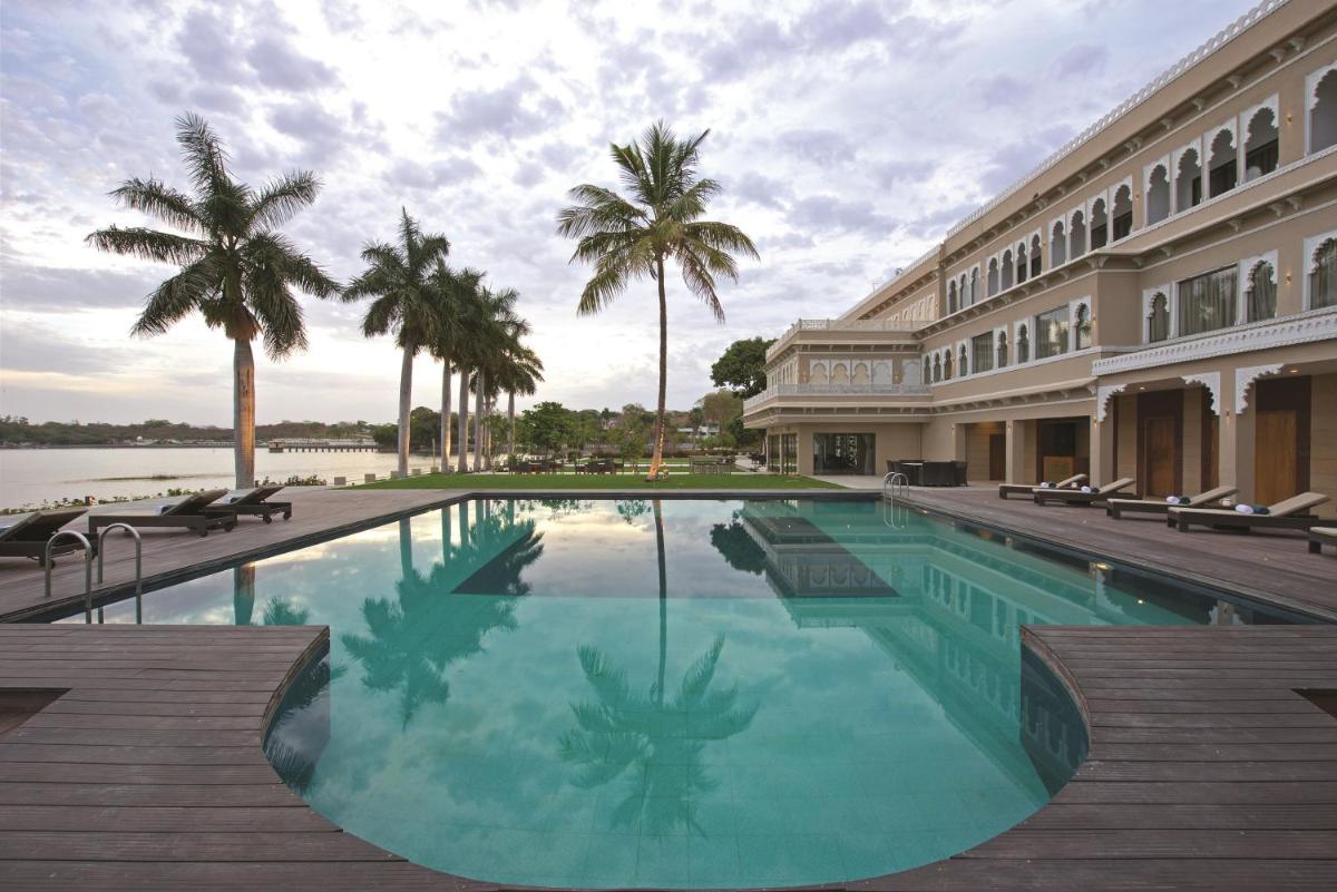 a large swimming pool next to a building with palm trees at Hotel Lakend in Udaipur