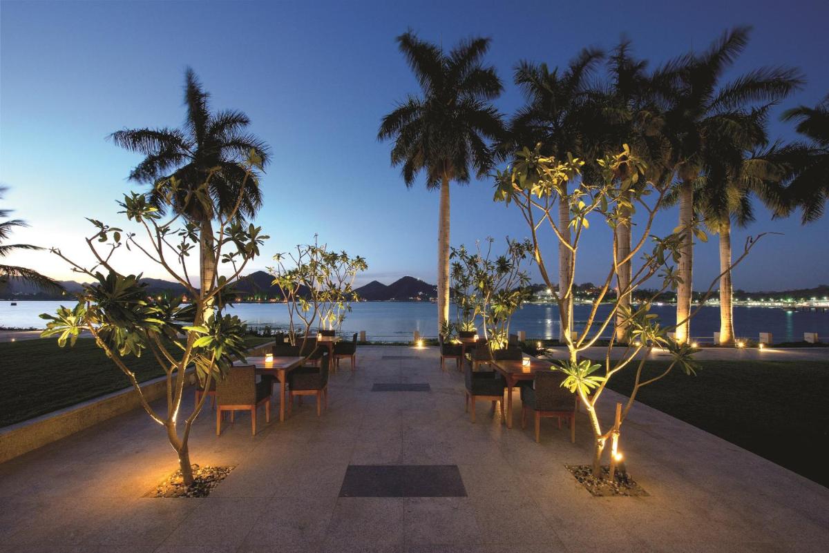 a patio with tables and chairs and palm trees at night at Hotel Lakend in Udaipur