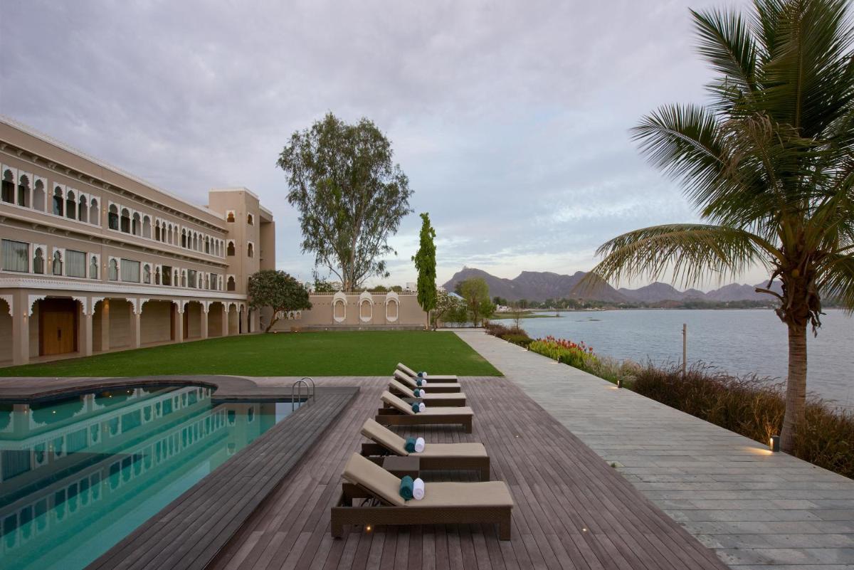 a building with a swimming pool next to a body of water at Hotel Lakend in Udaipur