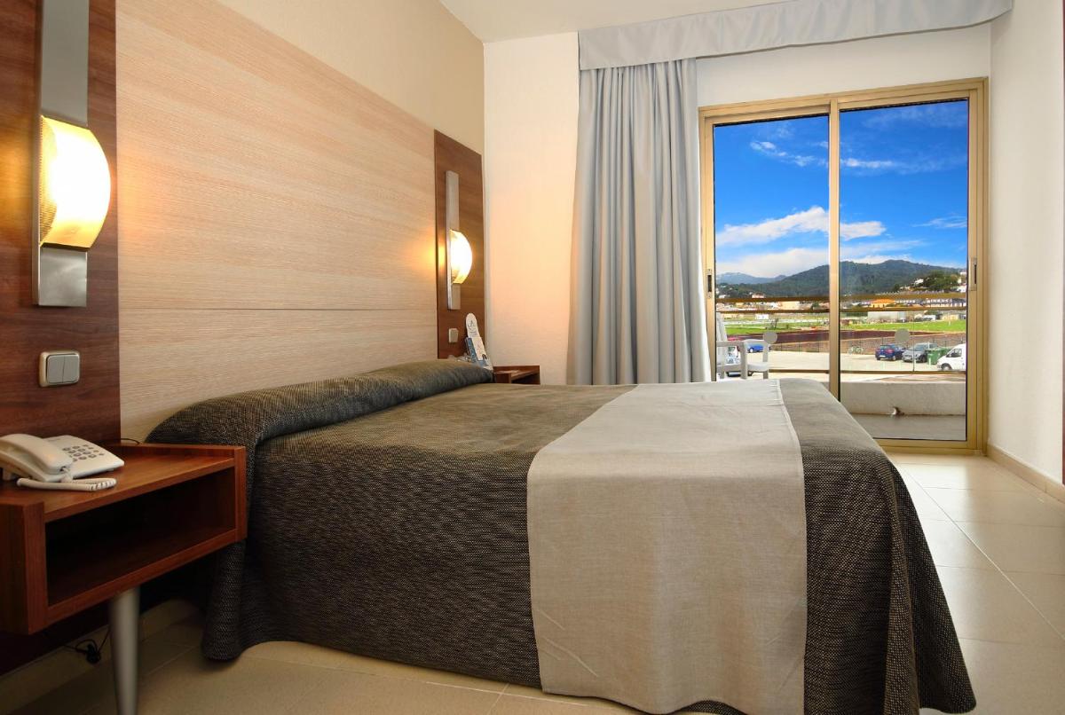 Una habitación de hotel con una cama y una ventana grande. en AQUA Hotel Aquamarina & Spa, en Santa Susanna Una habitación de hotel con una cama y una ventana grande. en AQUA Hotel Aquamarina & Spa, en Santa Susanna