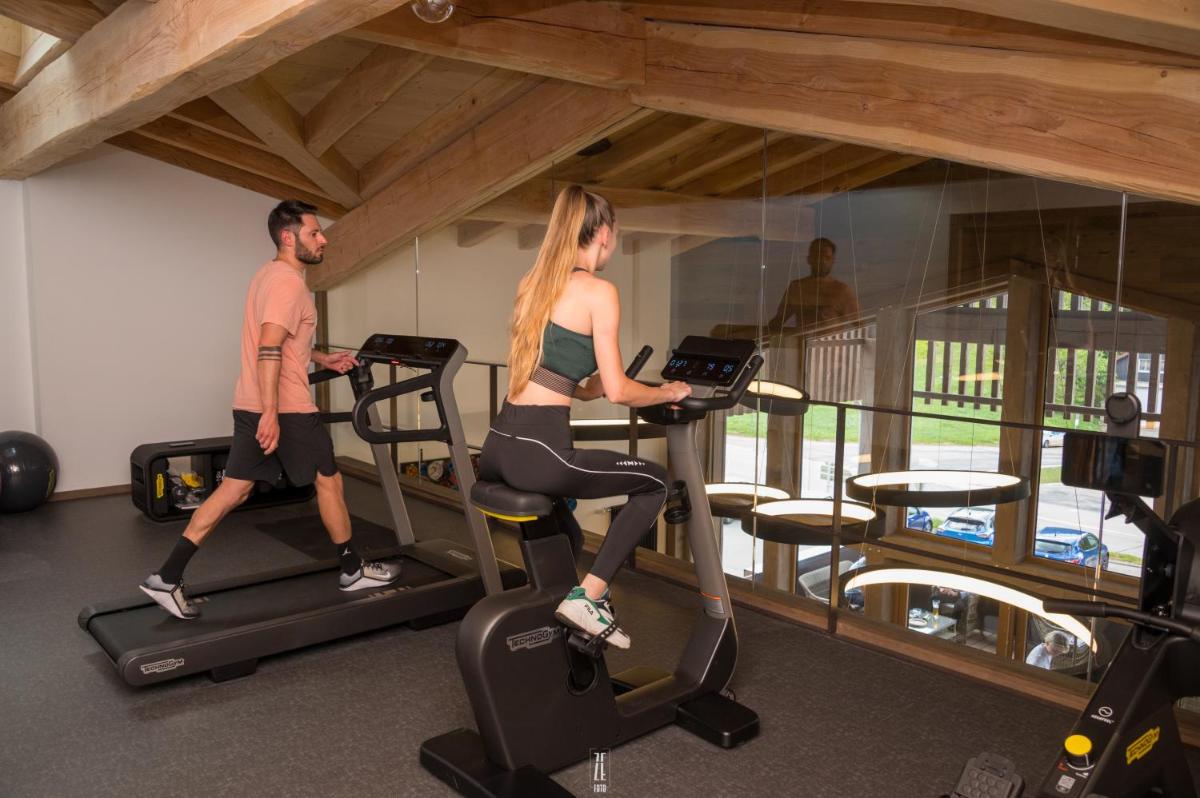 un homme et une femme font du vélo d'appartement dans une salle de sport dans l'établissement Chalet Hôtel & Spa Le Collet, à Xonrupt-Longemer