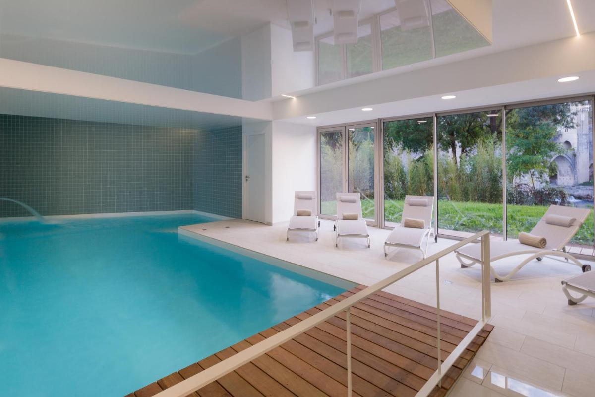 une piscine avec des chaises blanches dans une pièce dans l'établissement Best Western Plus Hotel Divona Cahors, à Cahors