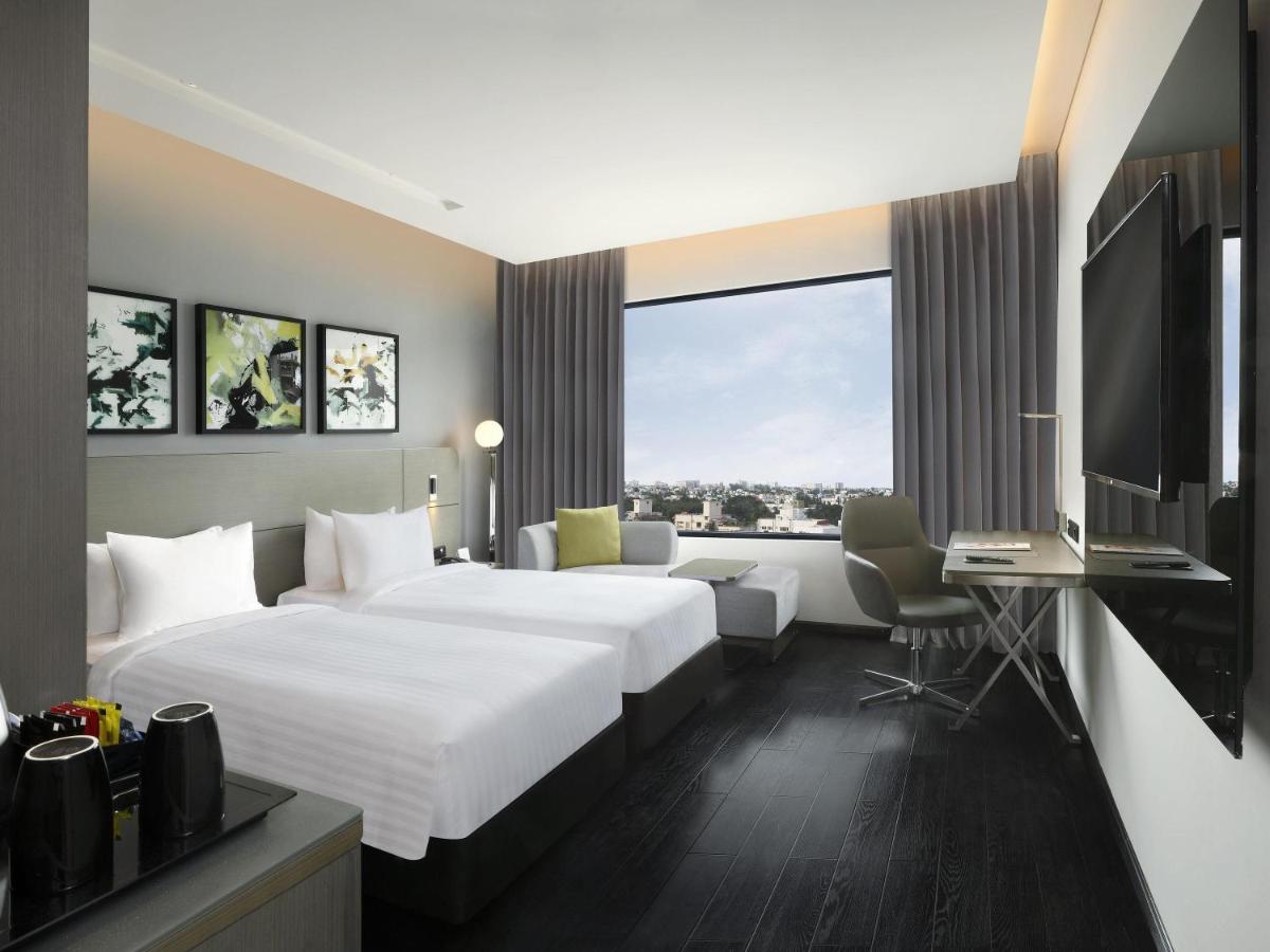 a hotel room with two beds and a desk at Novotel Chennai Chamiers Road in Chennai