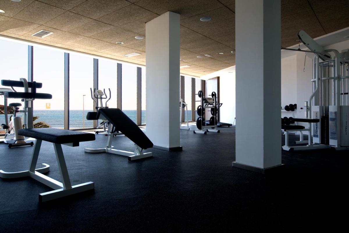 un gimnasio con equipo cardiovascular en una gran sala con ventanas en R2 Romantic Fantasia Suites - Adults Only, en Tarajalejo