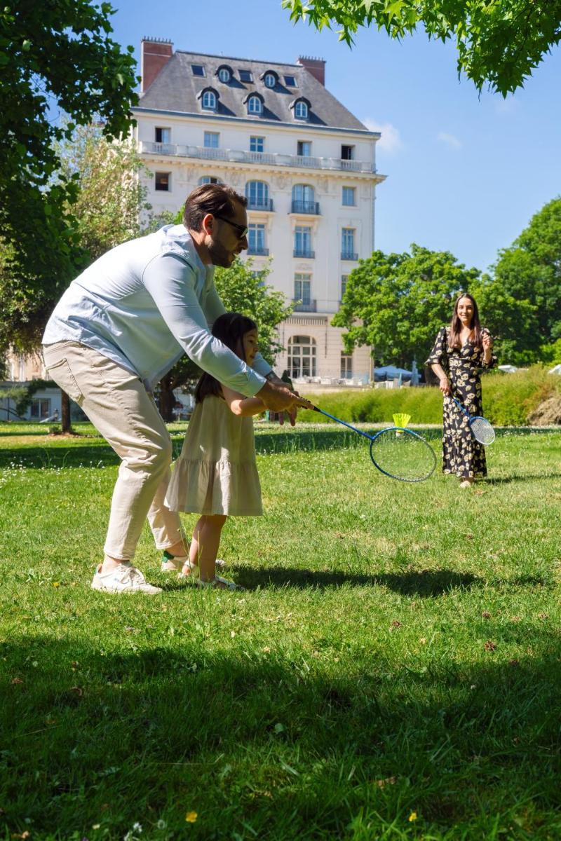 Un homme et une petite fille jouent avec une raquette de tennis. dans l'établissement Waldorf Astoria Versailles - Trianon Palace, à Versailles