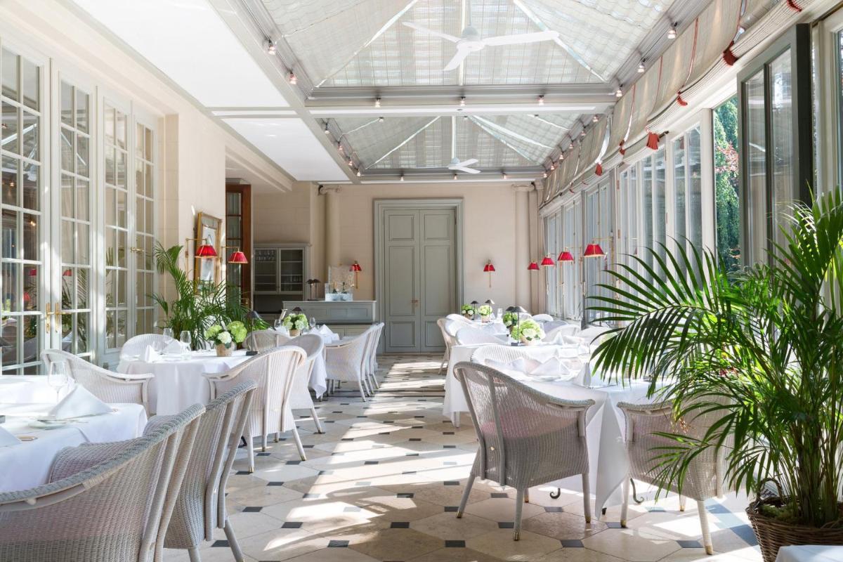 ein Restaurant mit weißen Tischen und Stühlen und Fenstern in der Unterkunft Brenners Park Hotel & Spa, Oetker Hotels in Baden-Baden