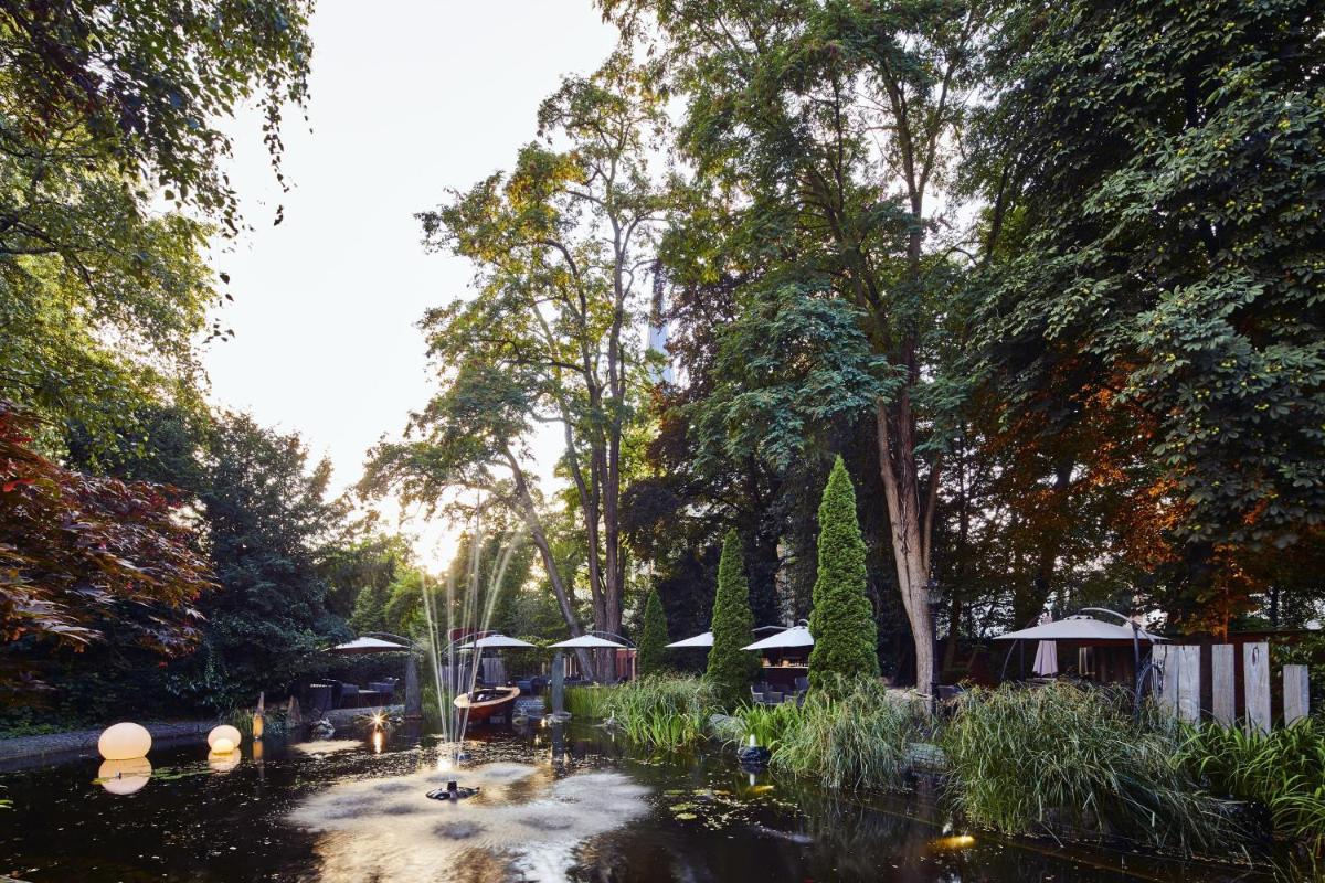 ein Teich mit einer Gruppe von Sonnenschirmen in einem Park in der Unterkunft Parkhotel Gütersloh in Gütersloh