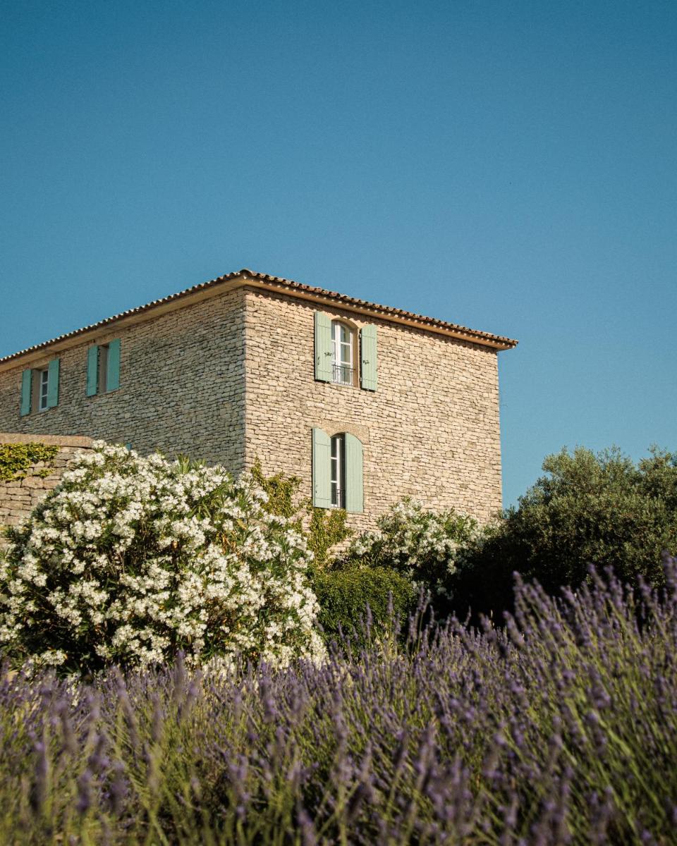un bâtiment en briques avec des fleurs blanches devant dans l'établissement Capelongue, a Beaumier hotel & Spa, à Bonnieux