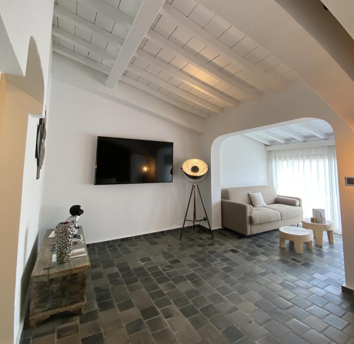 un salon avec un canapé et une télévision fixée au mur dans l'établissement Hôtel Le Roi Théodore & Spa, à Porto-Vecchio