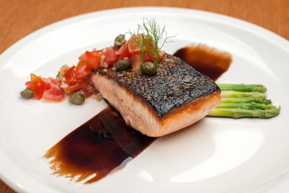 a white plate with a piece of fish and vegetables at Feathers- A Radha Hotel, Chennai in Chennai