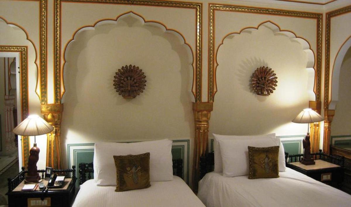 a bedroom with two beds with white sheets and golditures at The Raj Palace (Small Luxury Hotels of the World) in Jaipur