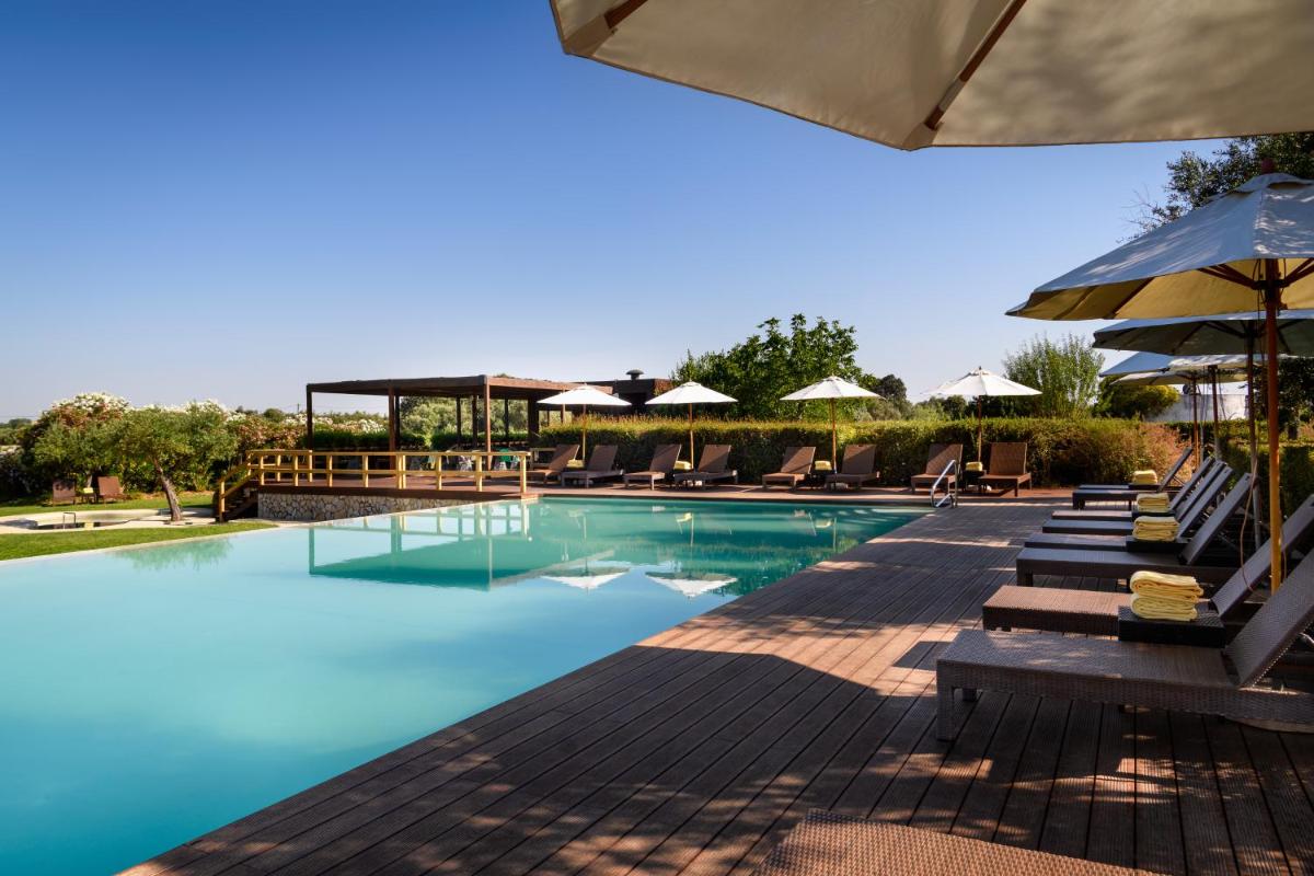 uma piscina com cadeiras e guarda-sóis em um resort em Convento do Espinheiro, Historic Hotel & Spa em Évora