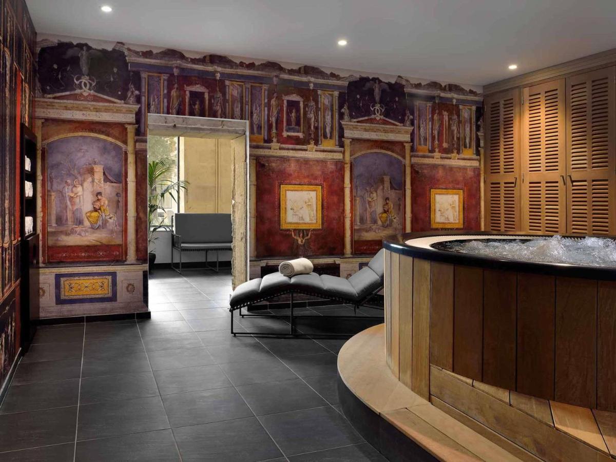 une salle de bains avec baignoire dans une pièce avec des tableaux dans l'établissement Jules César Hotel & Spa Arles - MGallery Collection, à Arles