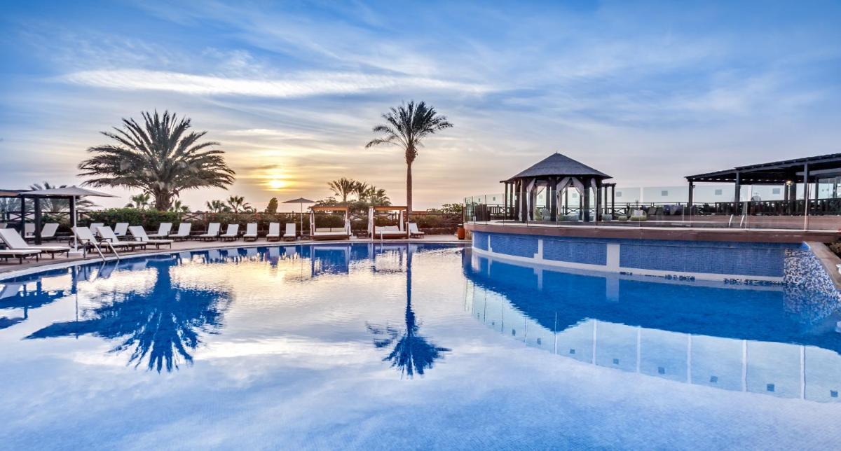 Una gran piscina con sillas y un cenador. en Occidental Jandía Royal Level - Adults Only, en Morro del Jable