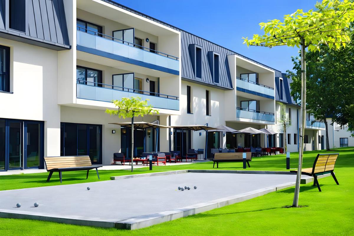 un immeuble d'appartements avec des bancs dans la cour dans l'établissement Les Boréales - Appart'hotel & Restaurant, à Villers-sur-Mer