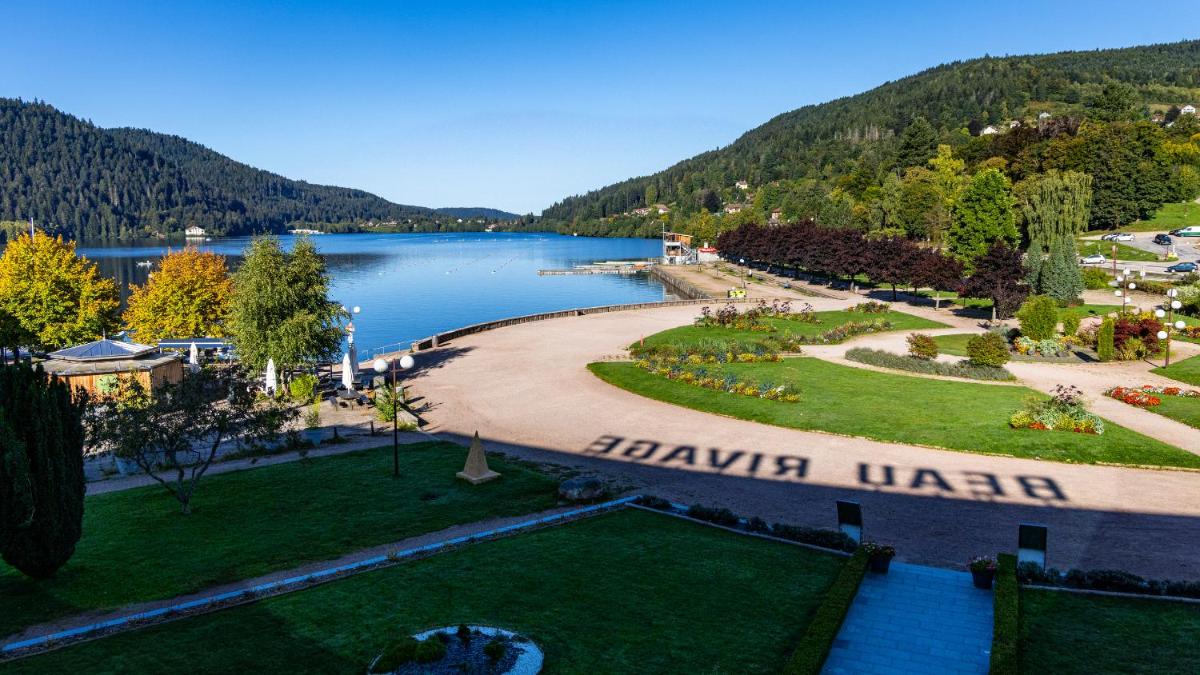une vue sur un parc avec un lac et des montagnes dans l'établissement Hôtel Beau Rivage, à Gérardmer