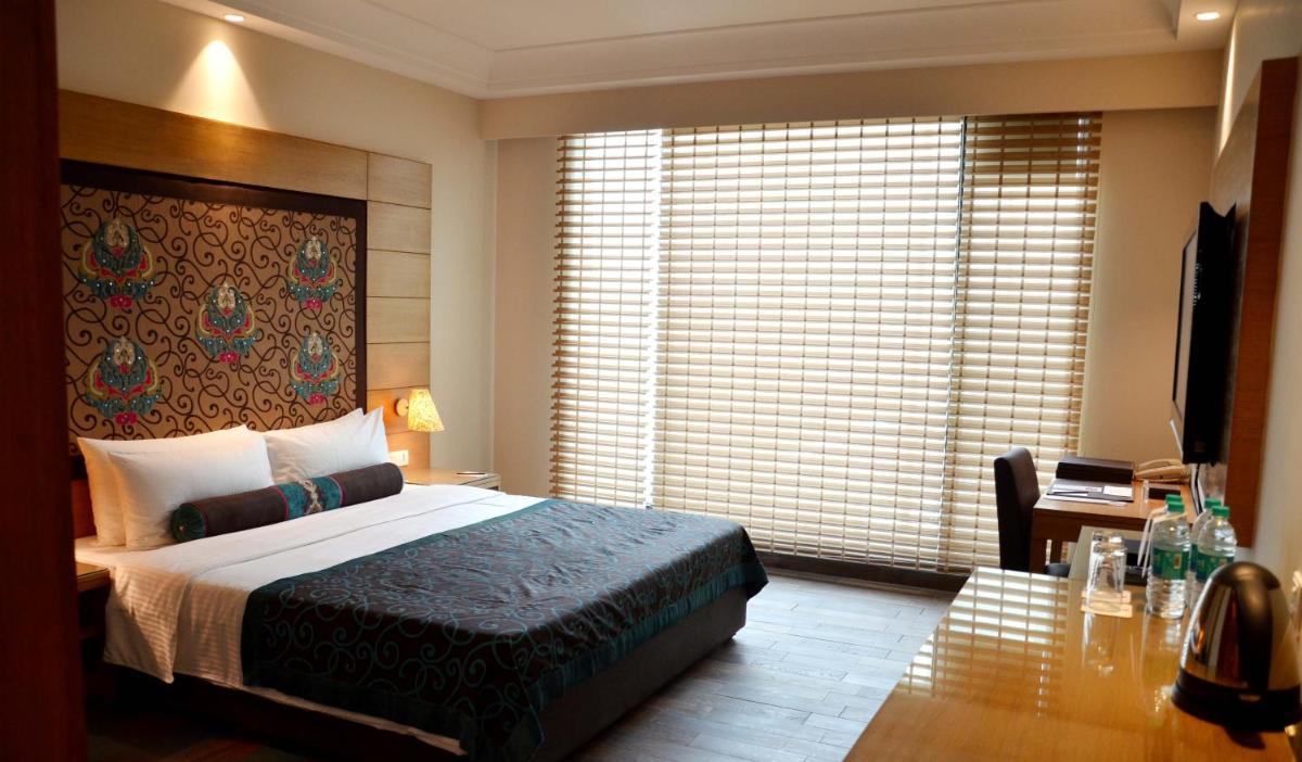 a bedroom with a bed and a desk and a window at The Lalit Jaipur in Jaipur