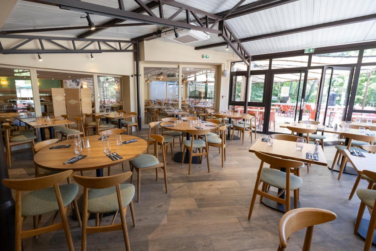 un restaurant avec des tables et des chaises en bois et des fenêtres dans l'établissement Club Vacances Bleues Domaine de Château Laval, à Gréoux-les-Bains
