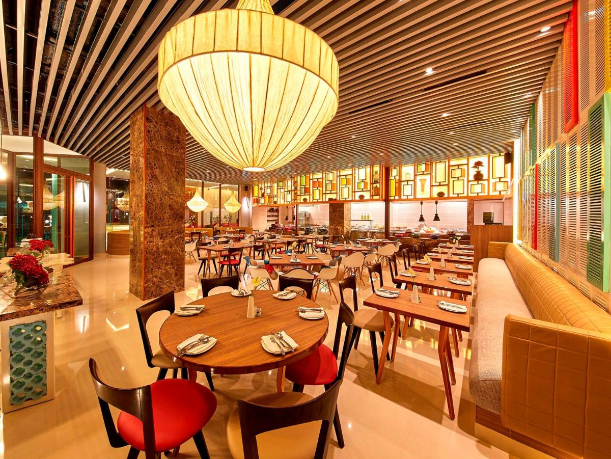 a restaurant with wooden tables and chairs and a large chandelier at Hotel Royal Orchid Bangalore in Bengaluru