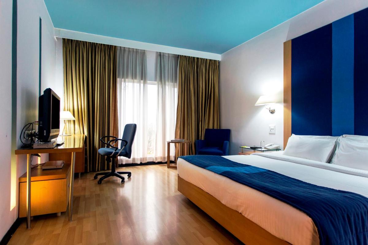 a hotel room with a bed and a desk and a television at Hotel Royal Orchid Bangalore in Bengaluru