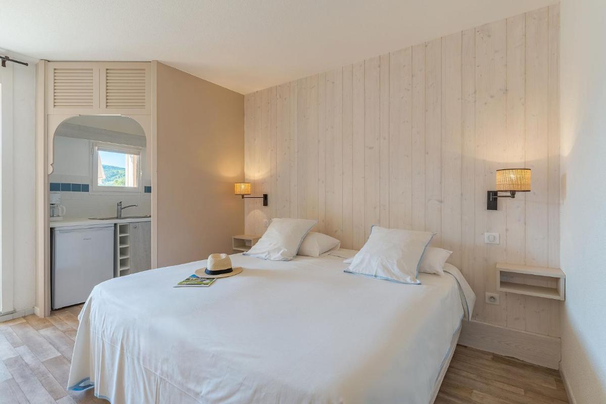 une chambre avec un lit blanc sur lequel il y a un chapeau dans l'établissement Résidence les Grands Pins, à Gréoux-les-Bains