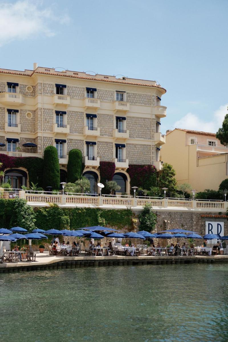 un hôtel avec des tables et des parasols bleus au bord de l'eau dans l'établissement Hôtel Belles Rives, à Juan-les-Pins