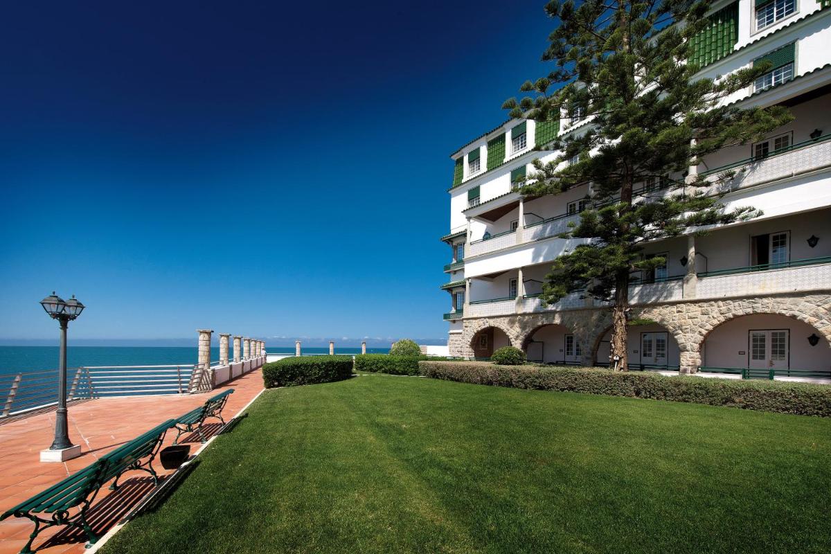 um banco de parque ao lado de um edifício com o oceano em Vila Gale Ericeira na Ericeira
