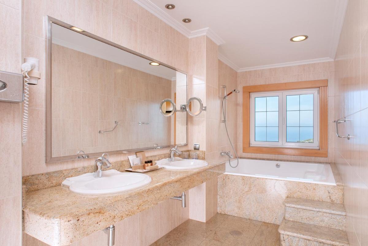 Un baño con dos lavabos, una bañera y un espejo. en Talaso Atlántico, en Mougás