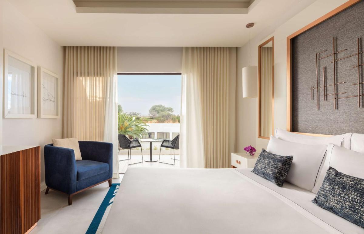 um quarto de hotel com uma cama e uma cadeira azul em Tivoli Carvoeiro em Carvoeiro um quarto de hotel com uma cama e uma cadeira azul em Tivoli Carvoeiro em Carvoeiro