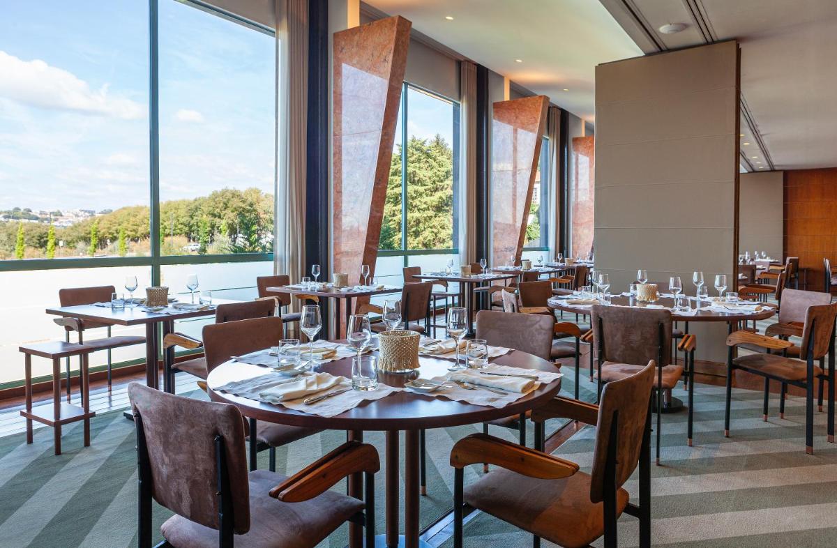 Um restaurante com mesas, cadeiras e janelas amplas. em Hotel de Guimaraes Business & SPA em Guimarães