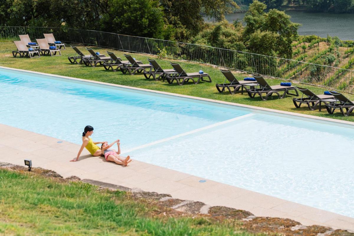 uma mulher sentada na borda de uma piscina em Douro Palace Hotel Resort & SPA em Baião