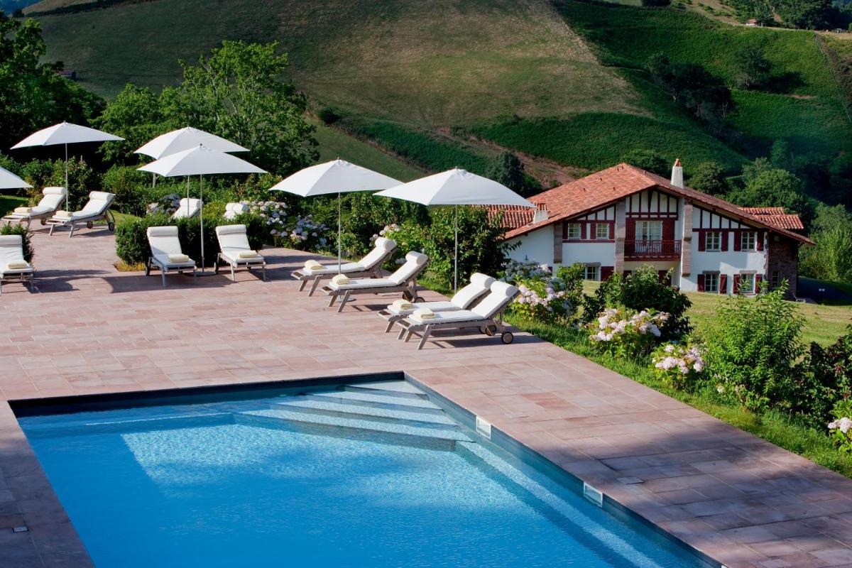 une piscine avec des chaises et des parasols ainsi qu'une maison dans l'établissement Auberge Ostapé, à Bidarray