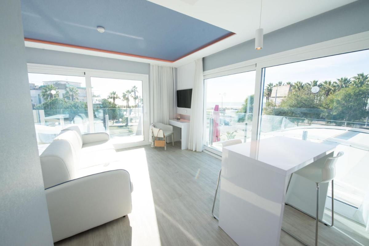 Una sala de estar con muebles blancos y una gran ventana. en Masd Mediterraneo Hotel Apartamentos Spa, en Castelldefels