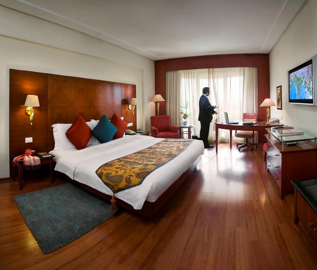 a man standing in a hotel room with a large bed at The Lalit Mumbai in Mumbai