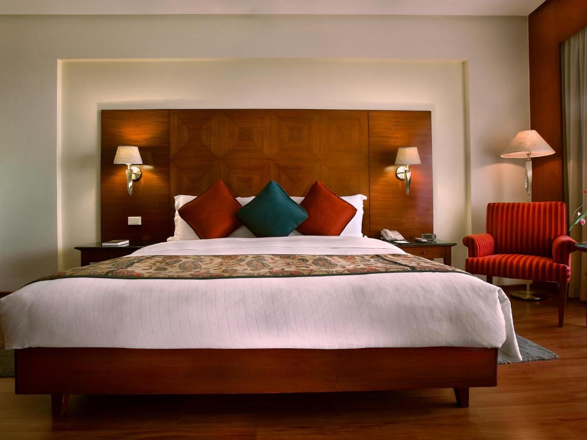 a bedroom with a large bed and a red chair at The Lalit Mumbai in Mumbai