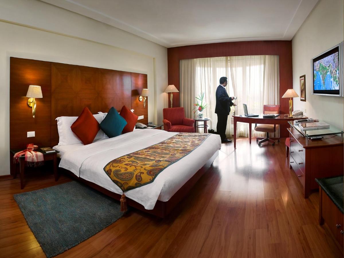 a man standing in a hotel room with a bed at The Lalit Mumbai in Mumbai