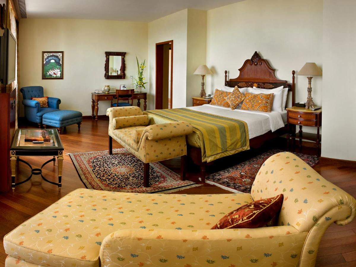 a bedroom with a bed and a couch and chairs at The Lalit Mumbai in Mumbai