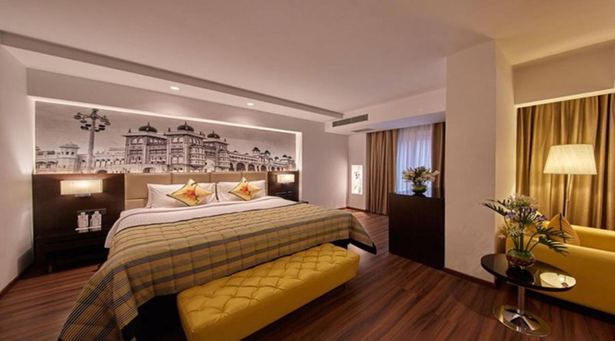 a hotel room with a large bed and a couch at Hotel Royal Orchid Bangalore in Bengaluru a hotel room with a large bed and a couch at Hotel Royal Orchid Bangalore in Bengaluru