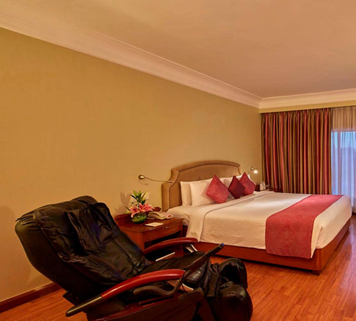 a hotel room with a bed and a chair at Hotel Royal Orchid Bangalore in Bengaluru