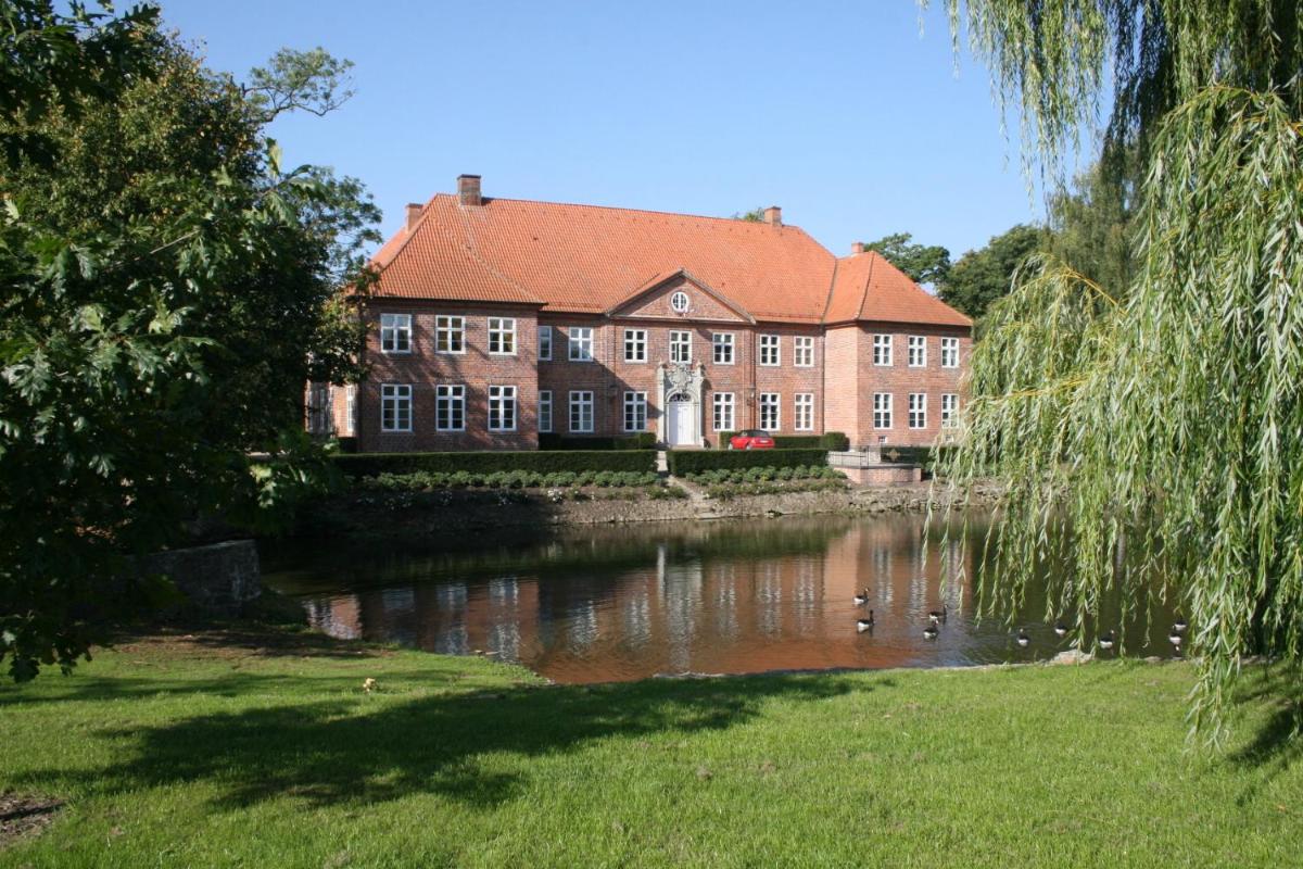 ein großes Backsteingebäude neben einem Gewässer in der Unterkunft Herrenhaus Borghorst in Osdorf