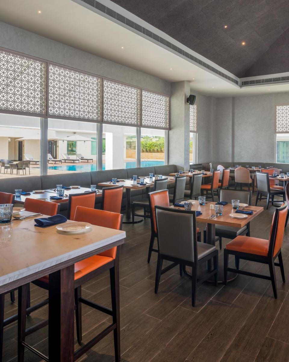 a dining room with tables and chairs and windows at The Residency Towers, Rameswaram in Rāmeswaram