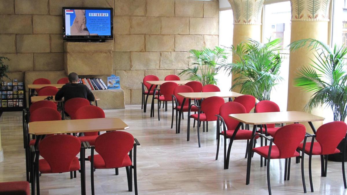 una habitación con sillas y mesas rojas y un hombre sentado en una mesa en Cleopatra Spa Hotel, en Lloret de Mar