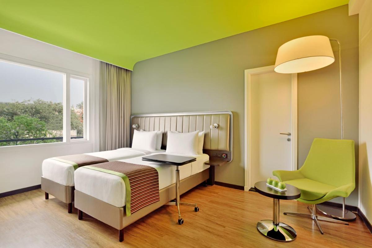 a bedroom with a bed and a desk and a window at Park Inn by Radisson,South Delhi in New Delhi a bedroom with a bed and a desk and a window at Park Inn by Radisson,South Delhi in New Delhi