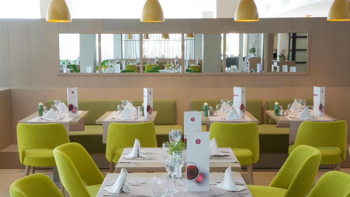 Un restaurante con mesas blancas y sillas verdes. en JS Alcudi-Mar, en Playa de Muro 104 fotos más