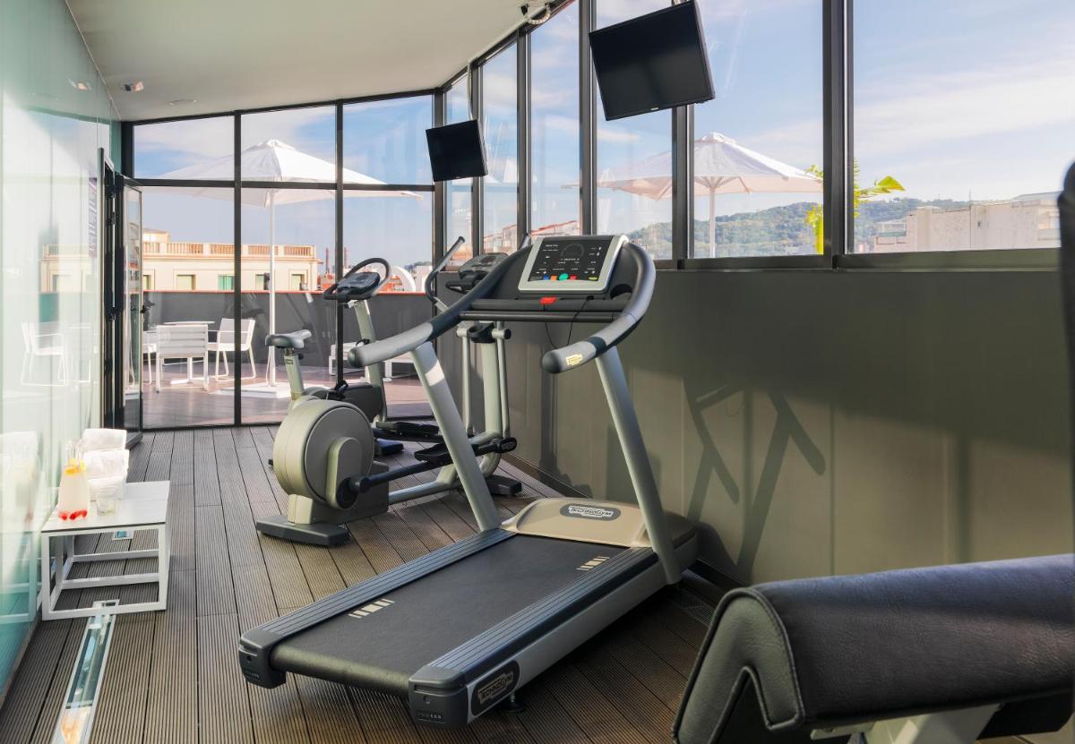 un gimnasio con cinta de correr en una habitación con ventanas en H10 Casanova, en Barcelona