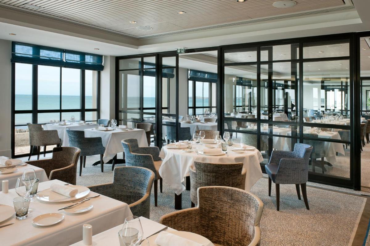 un restaurant avec des tables et des chaises blanches et des fenêtres dans l'établissement Hôtel Le Nouveau Monde, à Saint-Malo